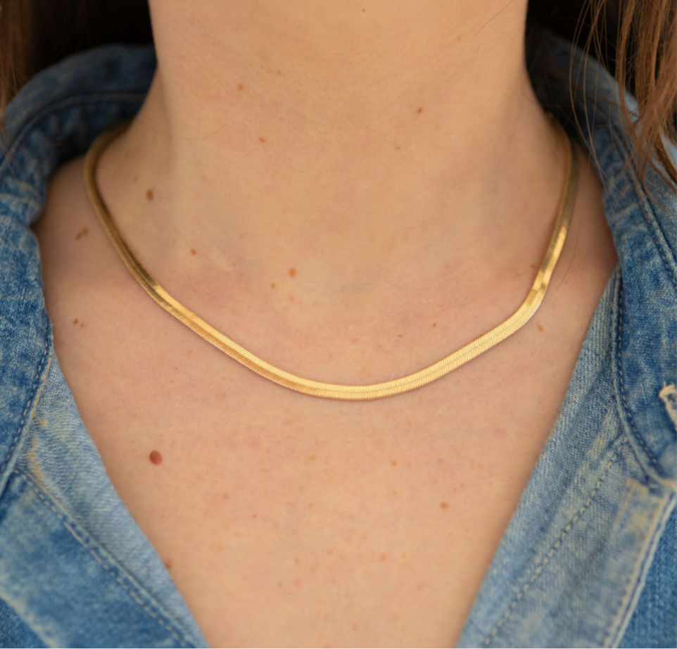 Gold herringbone chain necklace on a person wearing a button up denim shirt