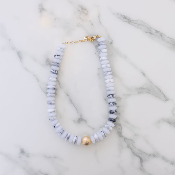 White and black marbled beaded necklace with a large textured gold bead at its center.