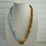 Picture of a bead necklace that is half light blue and half dark amber yellow. Necklace has a gold carabiner clasp.