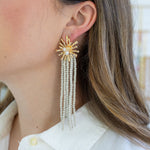 Picture of a gold starburst earrings with 5 shoulder length strands of white seed beads.