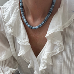 Person wearing a white blouse with ruffled details and a blue beaded necklace.