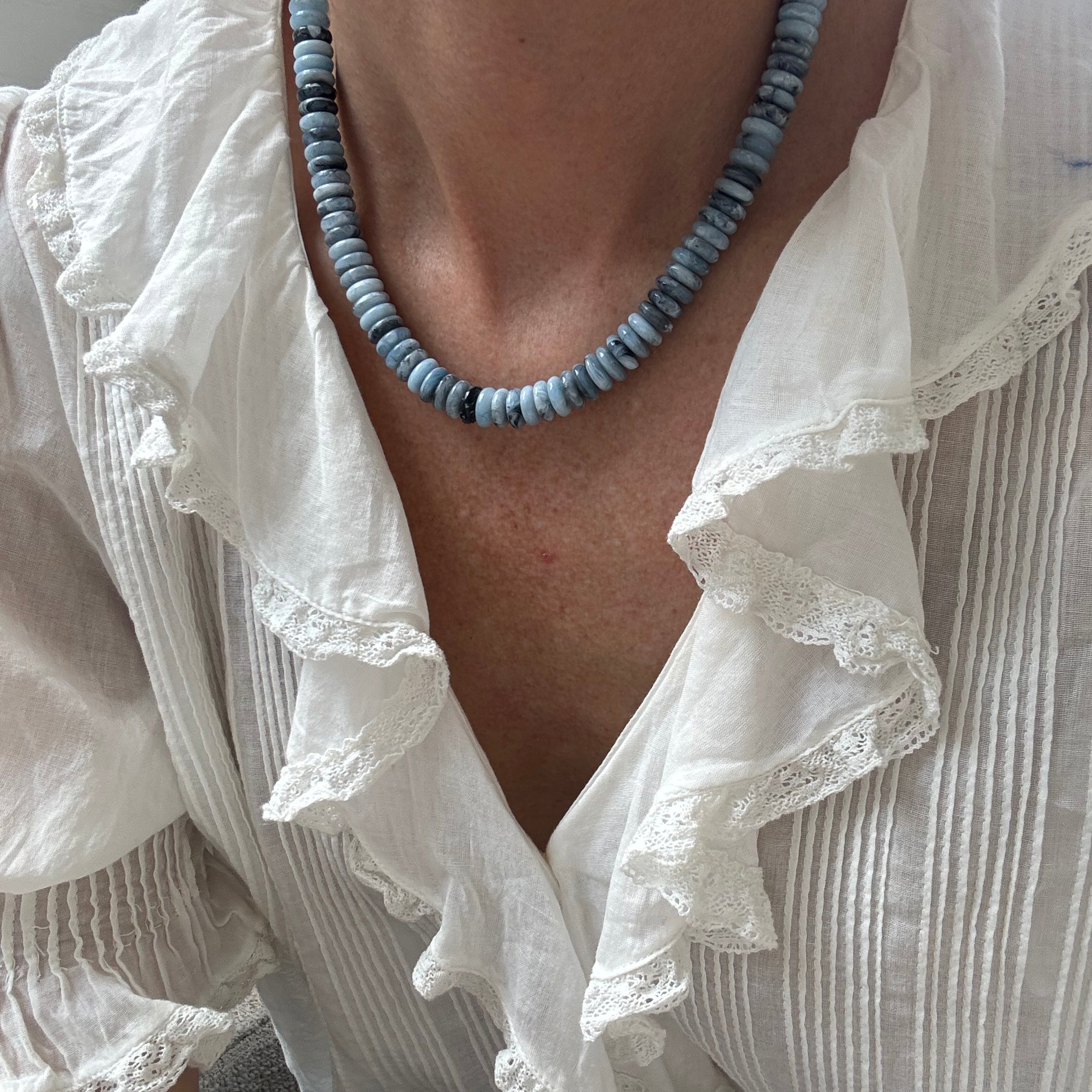 Person wearing a white blouse with ruffled details and a blue beaded necklace.