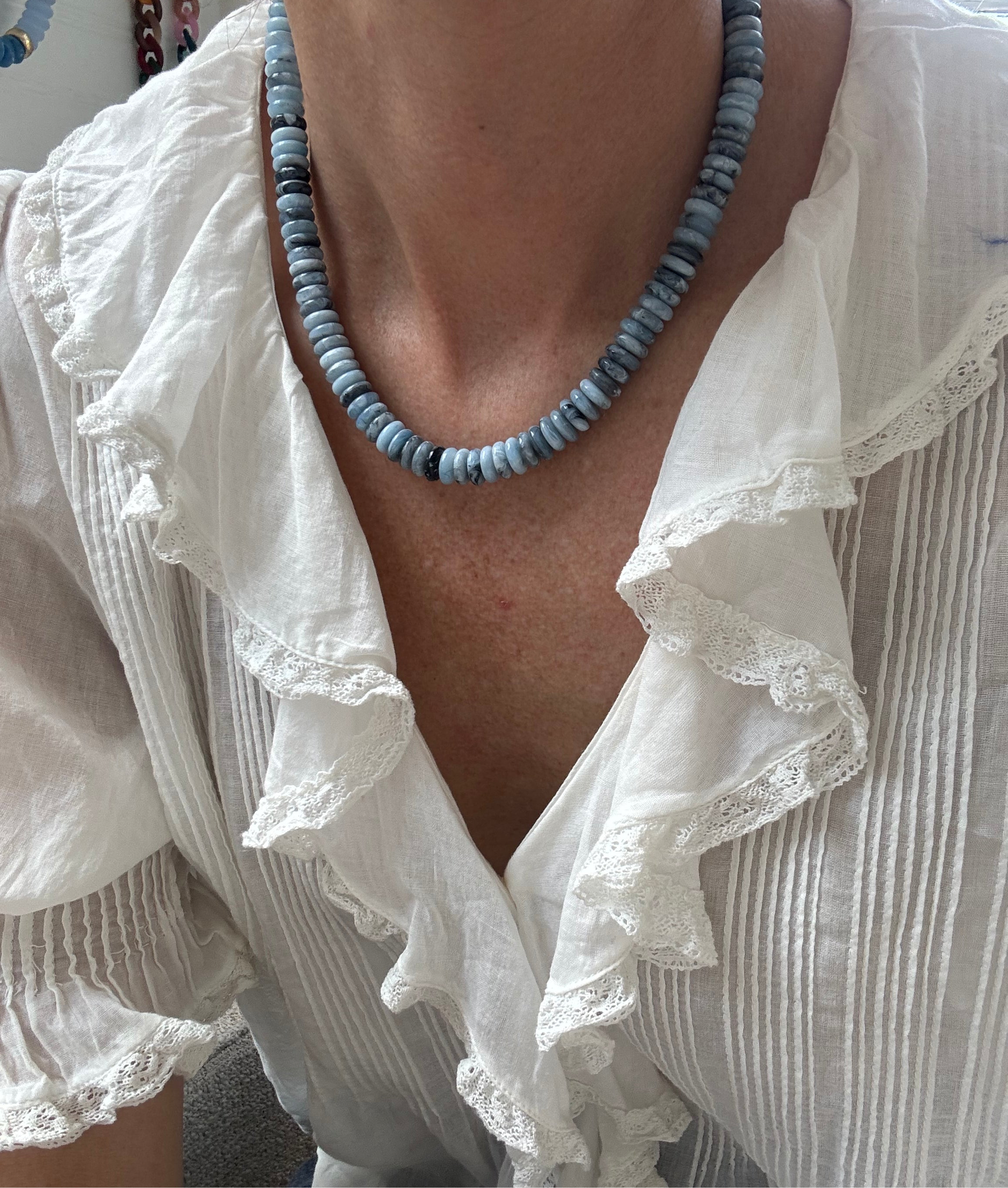Person wearing a white blouse with ruffled details and a blue beaded necklace.