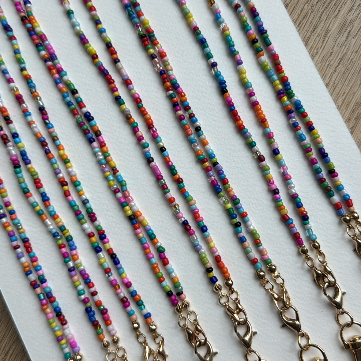 Picture of 8 multicolored beaded lanyards with gold clasps lined up next to each other.