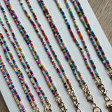 Picture of 8 multicolored beaded lanyards with gold clasps lined up next to each other.