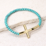 Turquoise beaded bracelet with a gold cross charm on a light background