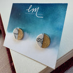 Picture of a pair of studs in a blue and white earring holder. Earrings are half white and black marble and half textured gold.