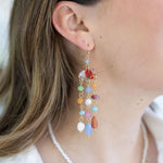 Woman wearing a colorful bead dangling earrings. Earring has beads in reds, blues, greens, oranges and whites.