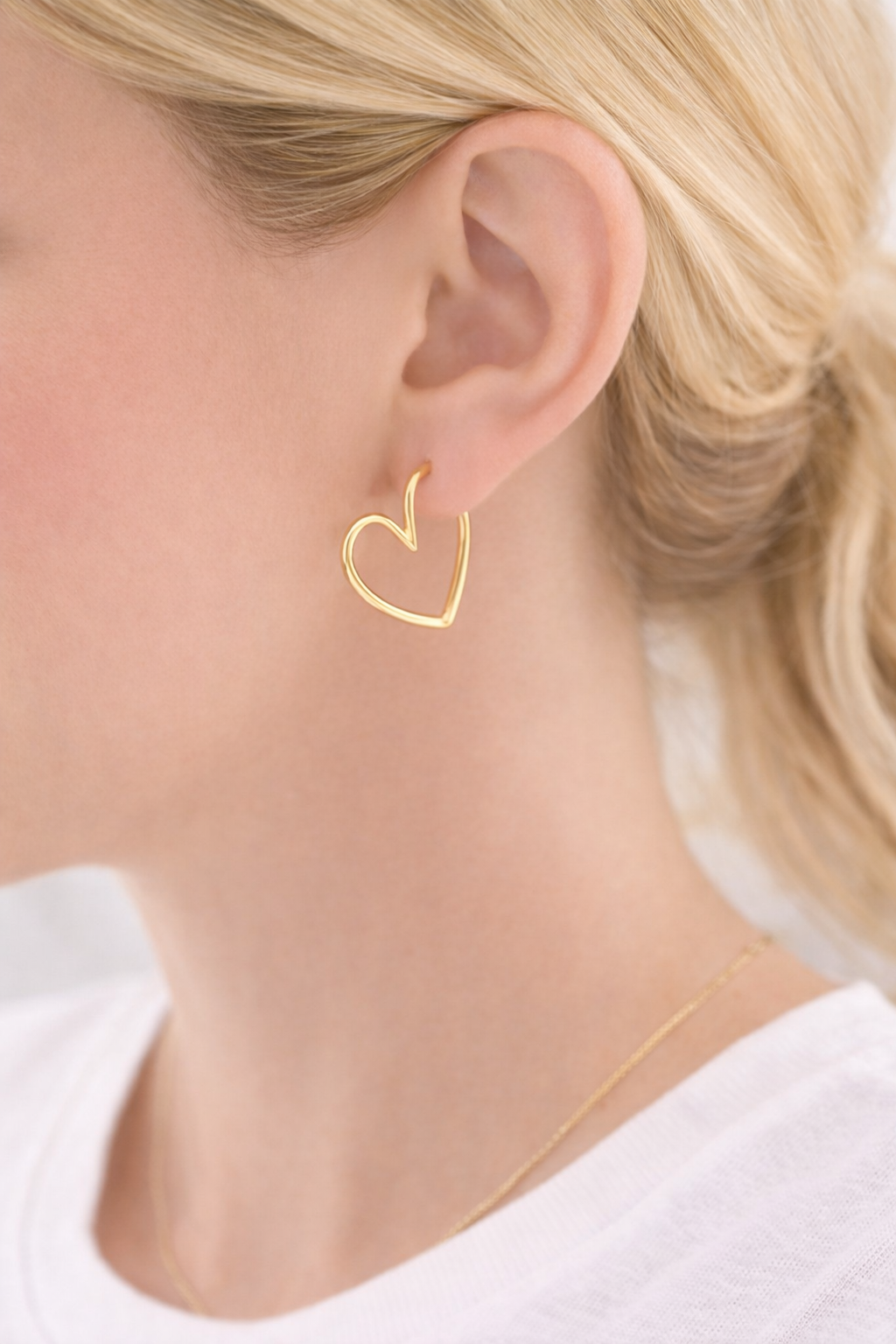Gold heart-shaped earring worn by a person with blonde hair.