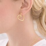 Gold heart-shaped earring worn by a person with blonde hair.