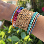 Picture of arm with 5 bracelets and one tan, woven cuff. Beaded bracelets are turquoise, coral, multicolored, blue and orange.