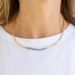 Picture of a dainty gold seed bead necklace with central blue, red and yellow beads.