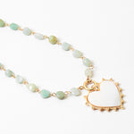 Picture of a necklace made of gold connectors and small light green stones. Necklace has a white enamel heart pendant.