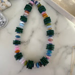 Colorful beaded necklace with dark green wooden disc beads on a marble surface