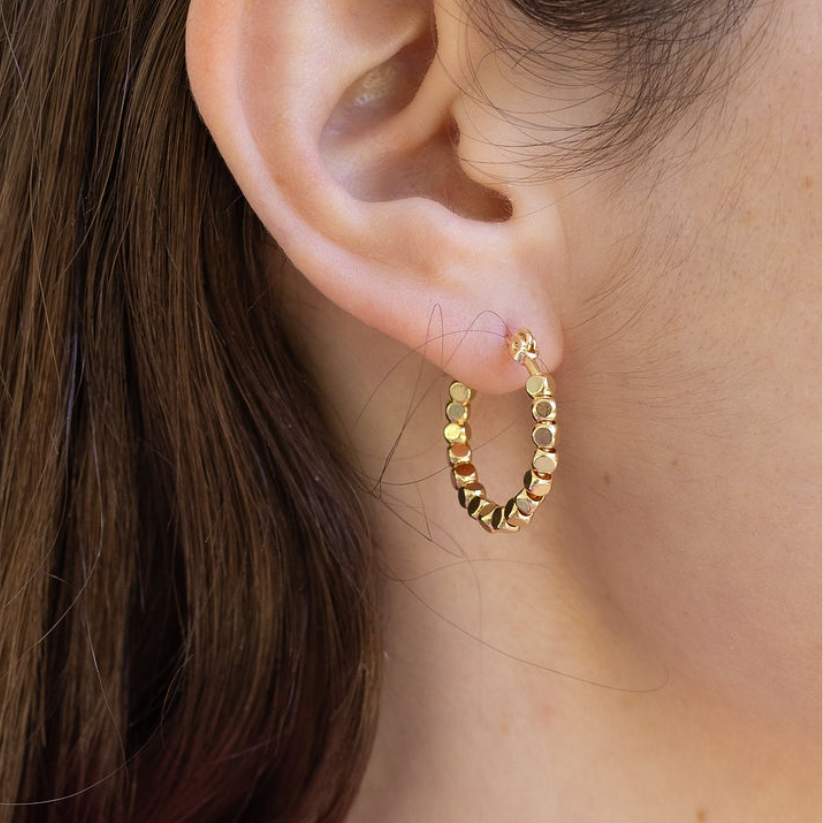 Gold hoop with square gold earrings worn by a person with brown hair.