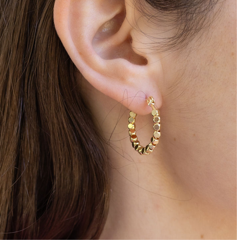 Gold hoop with square gold earrings worn by a person with brown hair.