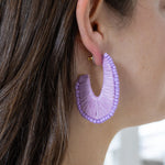 Model wearing a U-shaped hoop earrings covered by lavender thread and lavender colored beads.