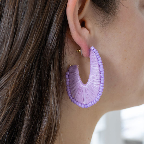 Model wearing a U-shaped hoop earrings covered by lavender thread and lavender colored beads.