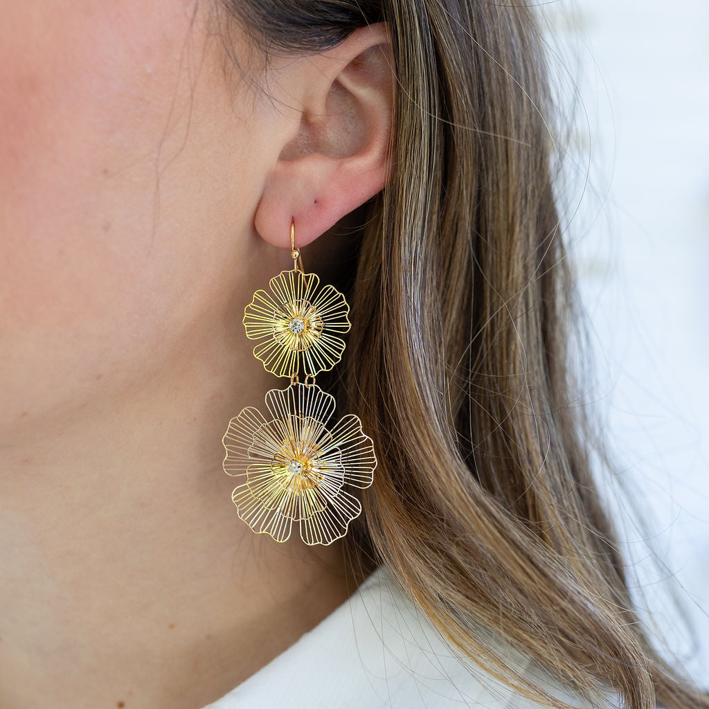 Woman wearing fine gold dangle flower earrings.