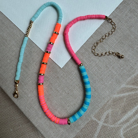 Picture of a necklace made of disc beads, gold accent beads and gold spacers. Disk beads are light blue, blue, bright orange and pink.