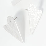 Set of two white geometric heart-shaped earrings on a light gray background