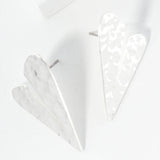 Set of two white geometric heart-shaped earrings on a light gray background
