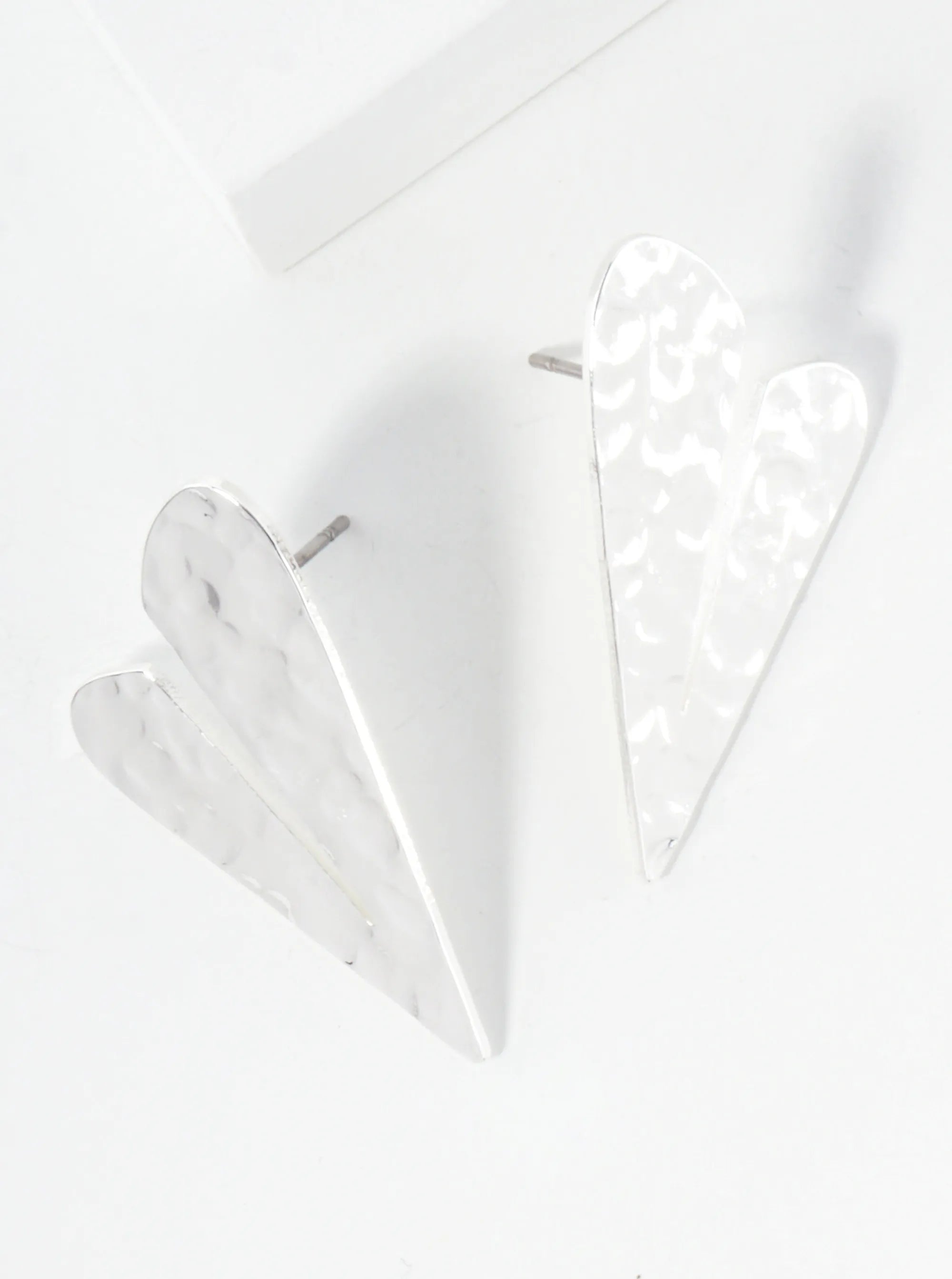Set of two white geometric heart-shaped earrings on a light gray background