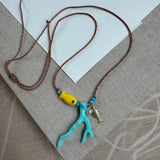 Picture of a woven string necklace with a yellow fish bead, a light blue coral bead, a fresh water pearl and a small gold fish pendant.
