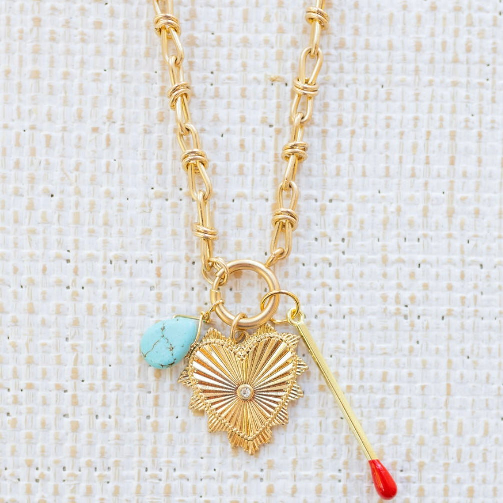 Picture of gold toggle chain with a turquoise teardrop, a large gold heart pendant with a diamond center and a gold matchstick.