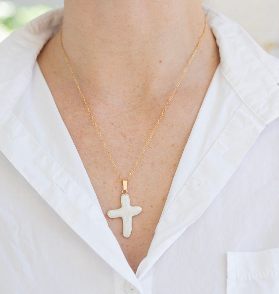 Gold necklace with a cross pendant worn by a person in a white shirt.