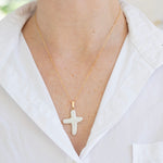 Gold necklace with a cross pendant worn by a person in a white shirt.