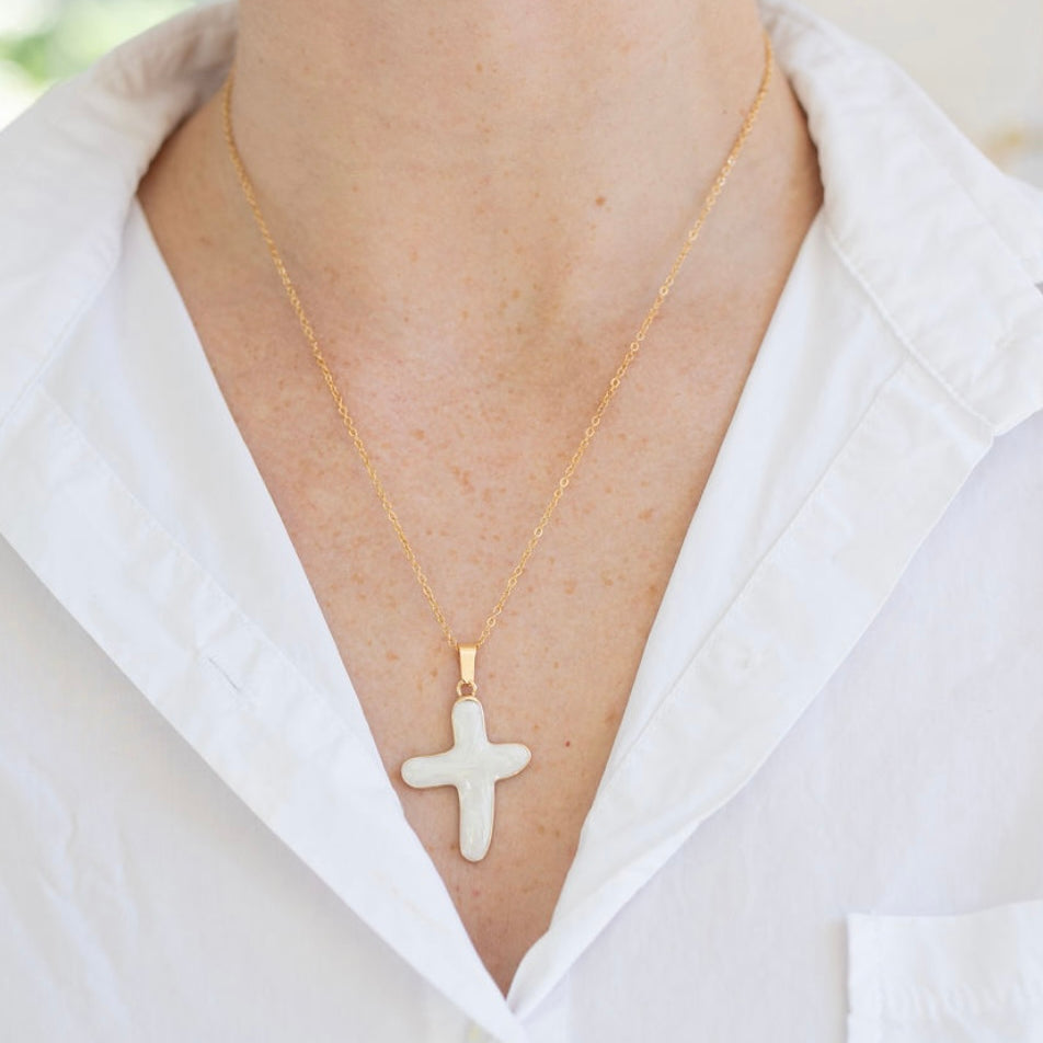 Gold necklace with a cross pendant worn by a person in a white shirt.