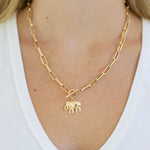 Gold chain necklace with an elephant pendant and toggle clasp worn by a person on a white background