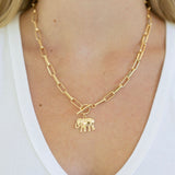Gold chain necklace with an elephant pendant and toggle clasp worn by a person on a white background