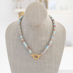 A semi-precious stone necklace with shades of baby blue, rust, and sand, featuring a gold carabiner clasp, displayed on a mannequin.