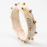 Picture of a marbled ivory colored bangle with inlaid gold beads.