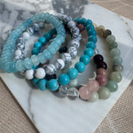 Set of colorful beaded bracelets on a marble surface. Bead bracelets are in blues, white marble, pinks and green