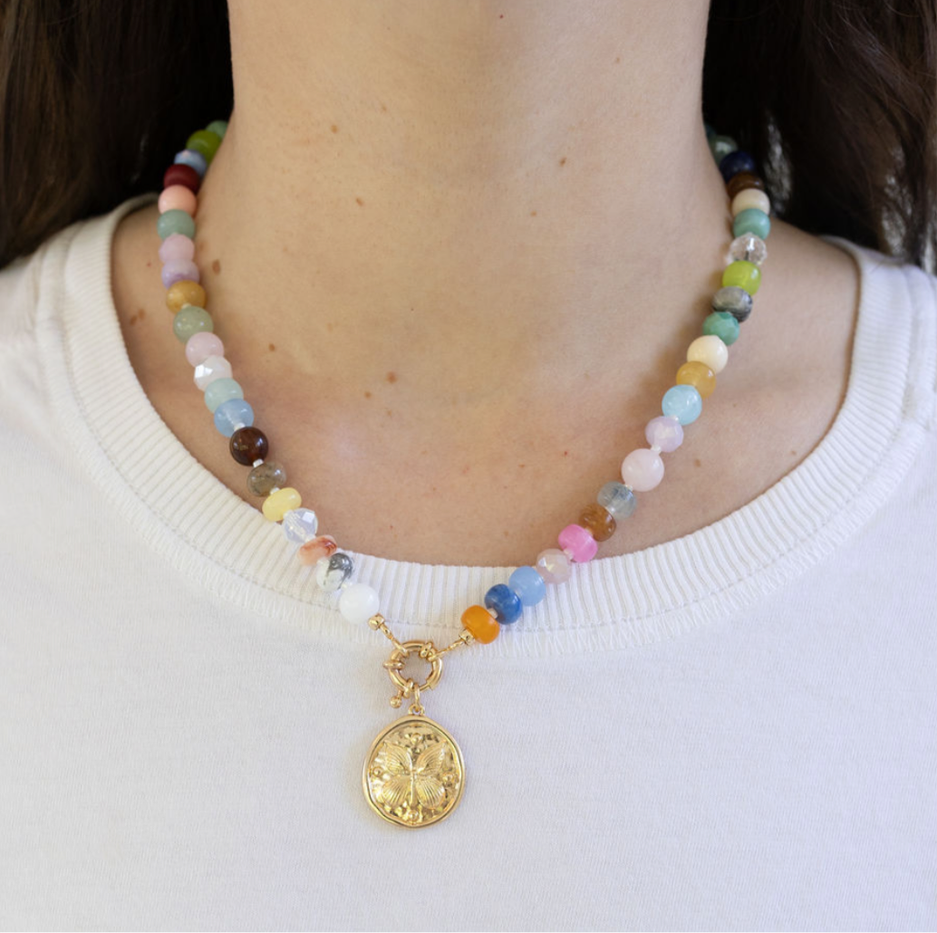 Multicolored beaded necklace with a gold butterfly disc pendant on a woman with a white shirt.
