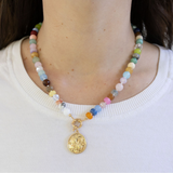 Multicolored beaded necklace with a gold butterfly disc pendant on a woman with a white shirt.