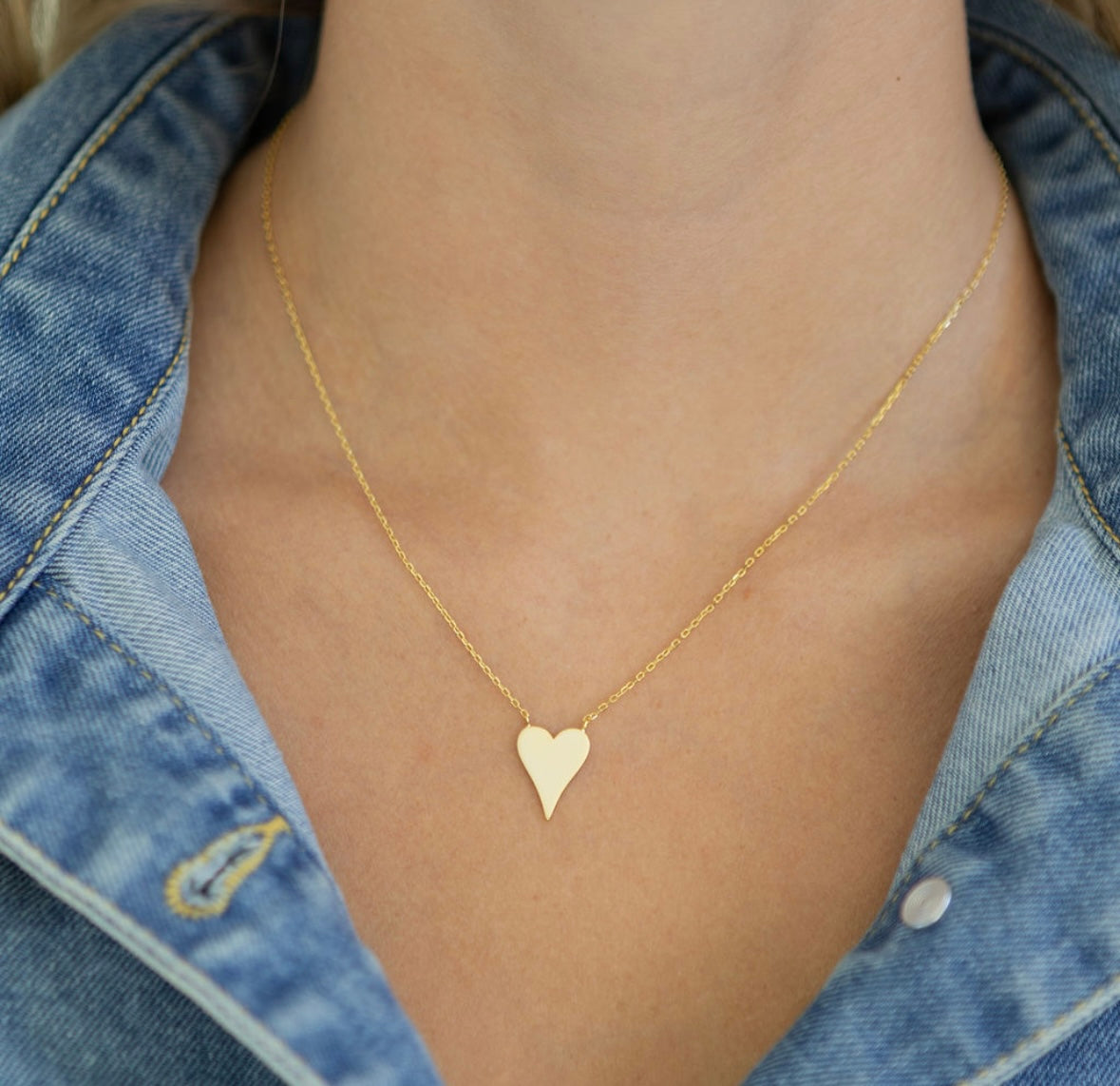 Dainty gold heart necklace worn by a person with a denim jacket.