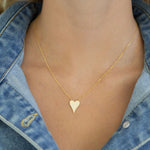 Dainty gold heart necklace worn by a person with a denim jacket.