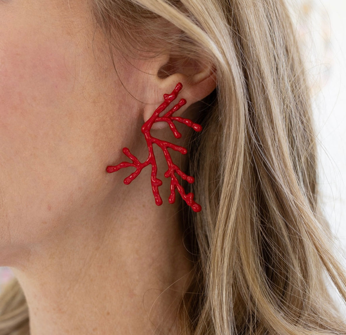 Red coral-shaped earrings worn by a person with blonde hair.