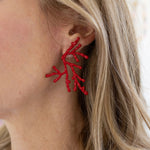 Red coral-shaped earrings worn by a person with blonde hair.