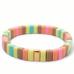 Colorful bracelet in pastel yellows, corals and browns with gold beads on a white background