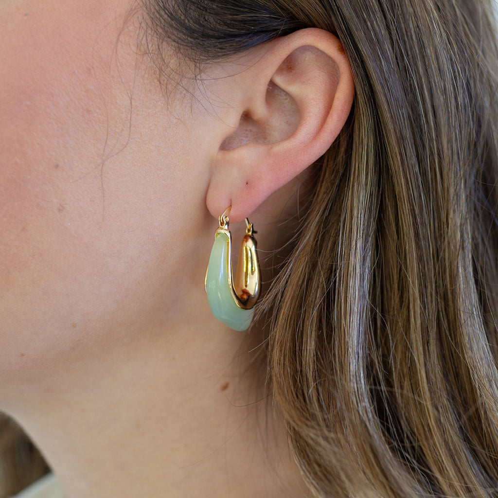 Picture of woman wearing light green resin hoops with gold on the inside arc.