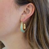 Picture of woman wearing light green resin hoops with gold on the inside arc.