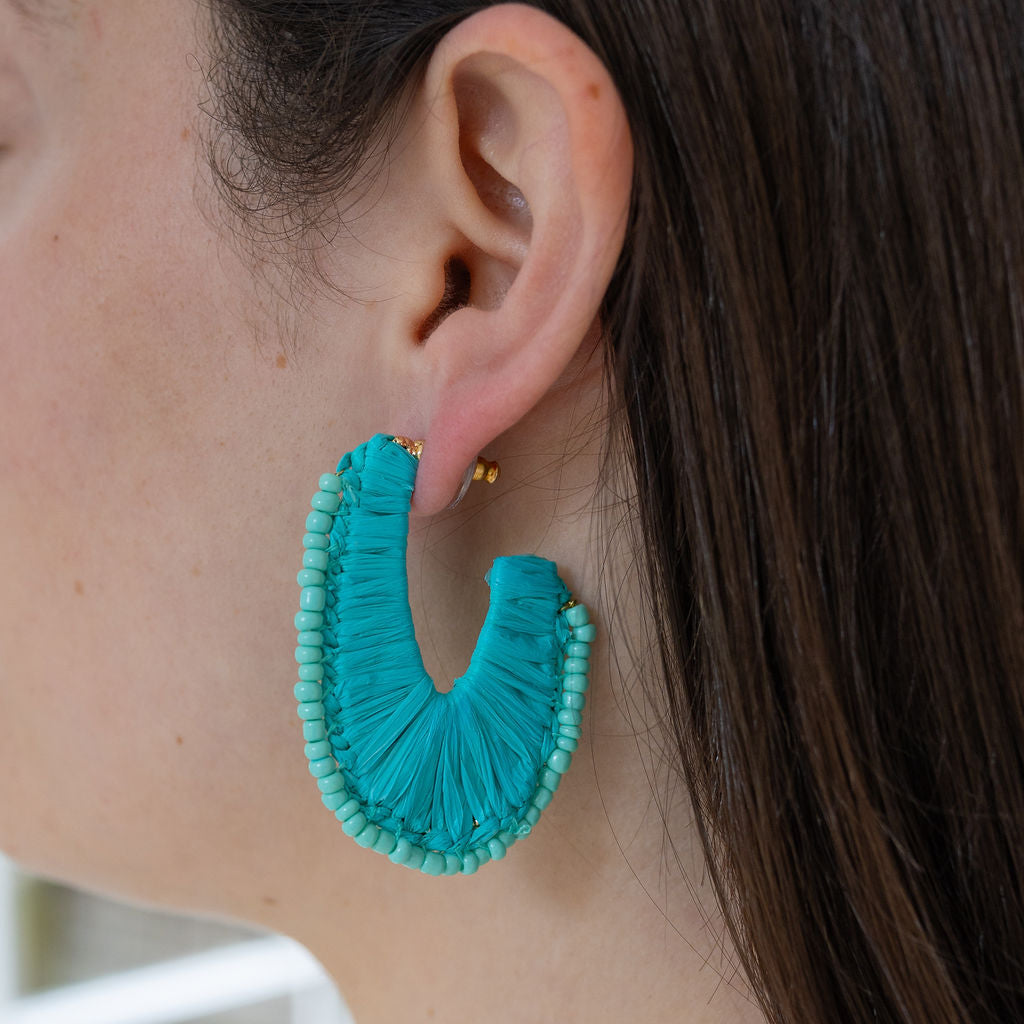 Picture of model wearing a U-shaped hoop earrings covered in blue cord and blue beads.