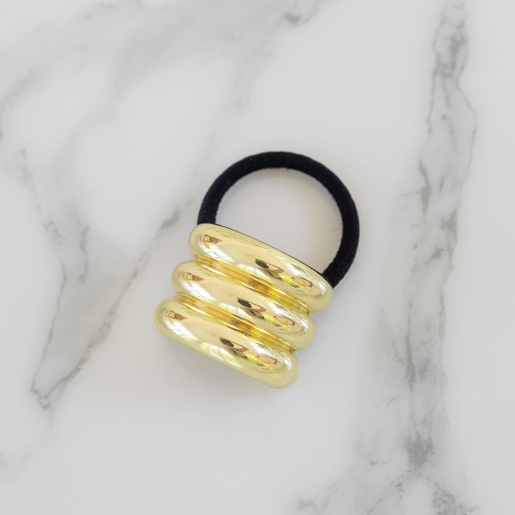 Black hair tie with gold spiral design on a marble background