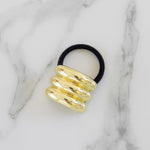 Black hair tie with gold spiral design on a marble background