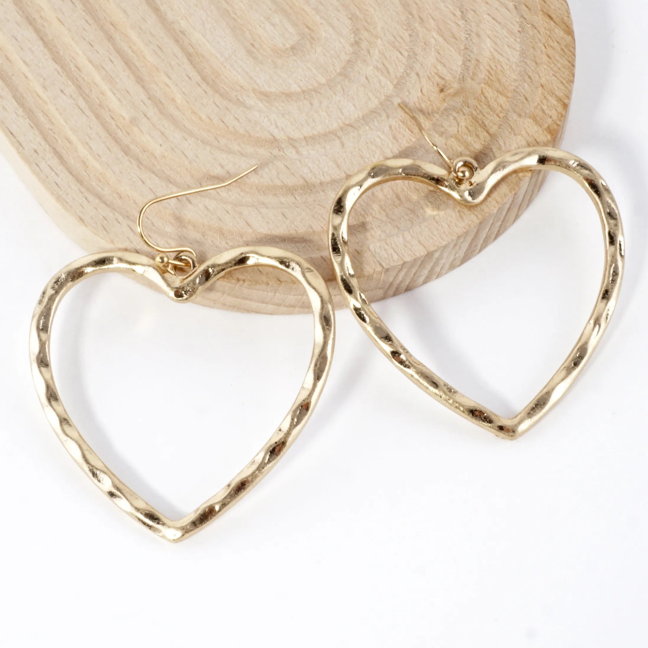Gold heart-shaped earrings on a wooden block with a white background